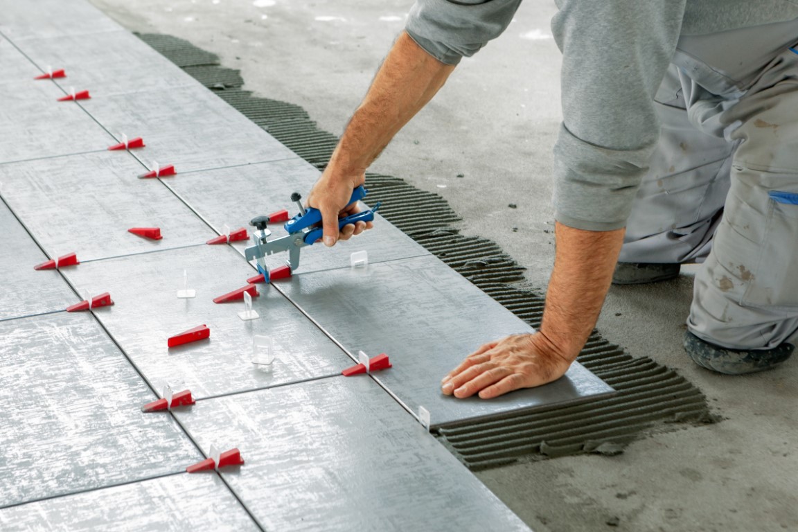 Ceramic Tiles. Tiler placing ceramic wall tile in position over adhesive with lash tile leveling system - Image