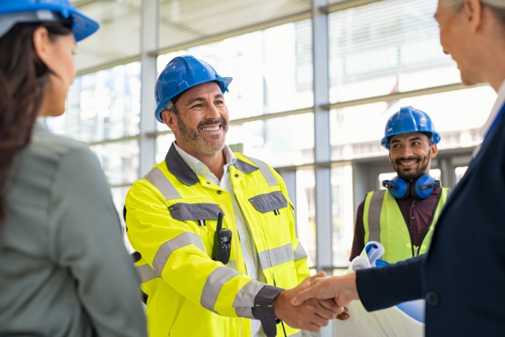 Smiling civil engineer shaking hands at construction site with happy business woman. Construction manager and supervisor shaking hand on building site. Team of workers conclude an agreement with an handshake.